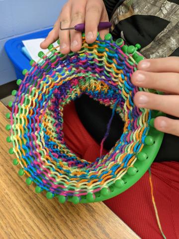 A circular knitting loom with multicolored yarn strung on for a hat in progress