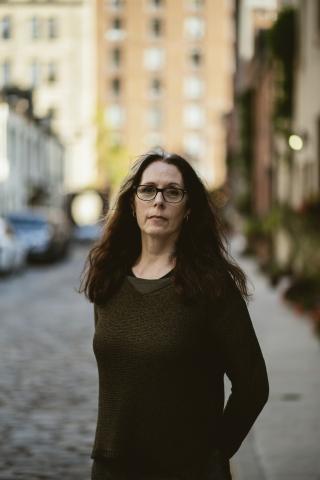 A woman with long dark hair, wearing glasses.