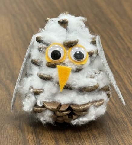 A pinecone that has been decorated to look like a snowy owl.