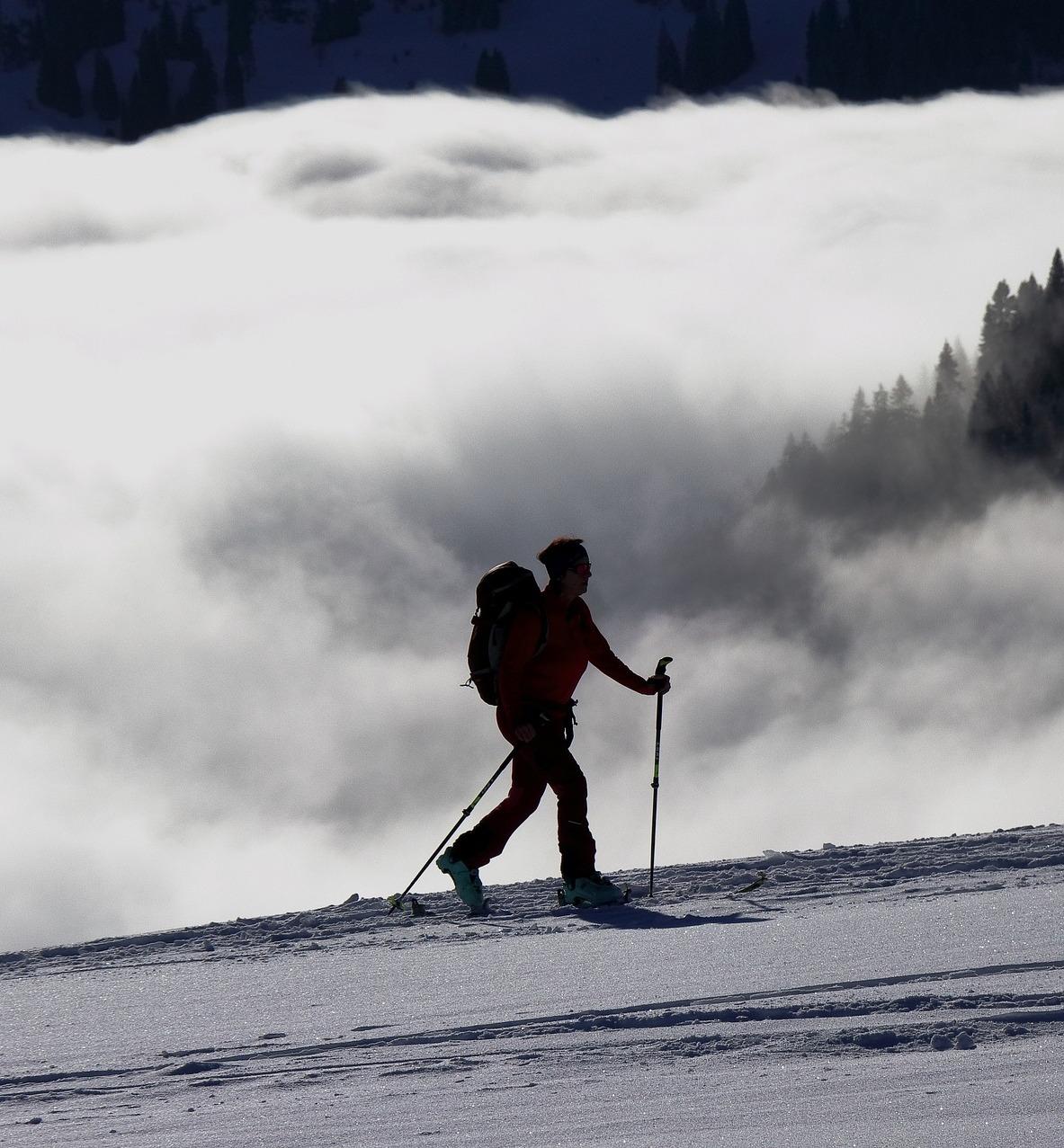 Silhouette of a cross-country skier skiing across a mountaintop, trees shrouded in clouds in the background