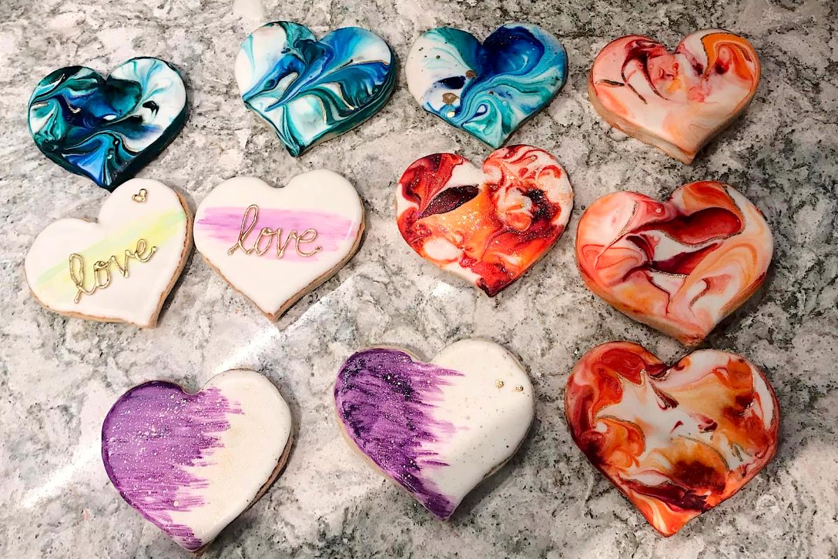 A dozen heart-shaped sugar cookies with a variety of decorative frosting designs.