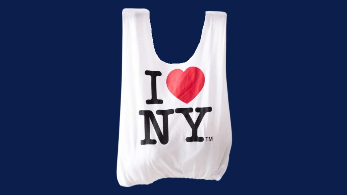 A white tote bag on a navy blue background.  The tote bag has "I (heart emoji) NY" on it